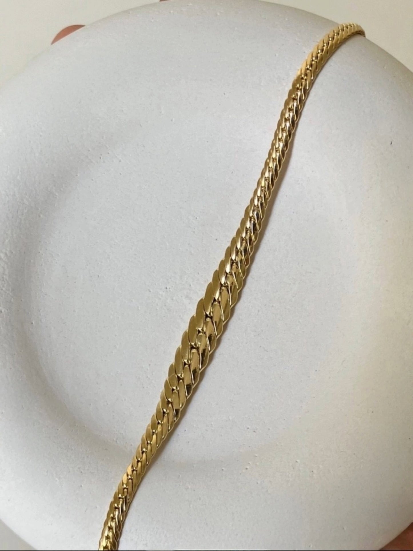 Elegantes Armband aus 18 Karat Gelbgold mit flach anliegenden, geflochten wirkenden Gliedern in hochglanzpolierter Verarbeitung, dekorativ auf einer runden, weißen Präsentationsfläche arrangiert.