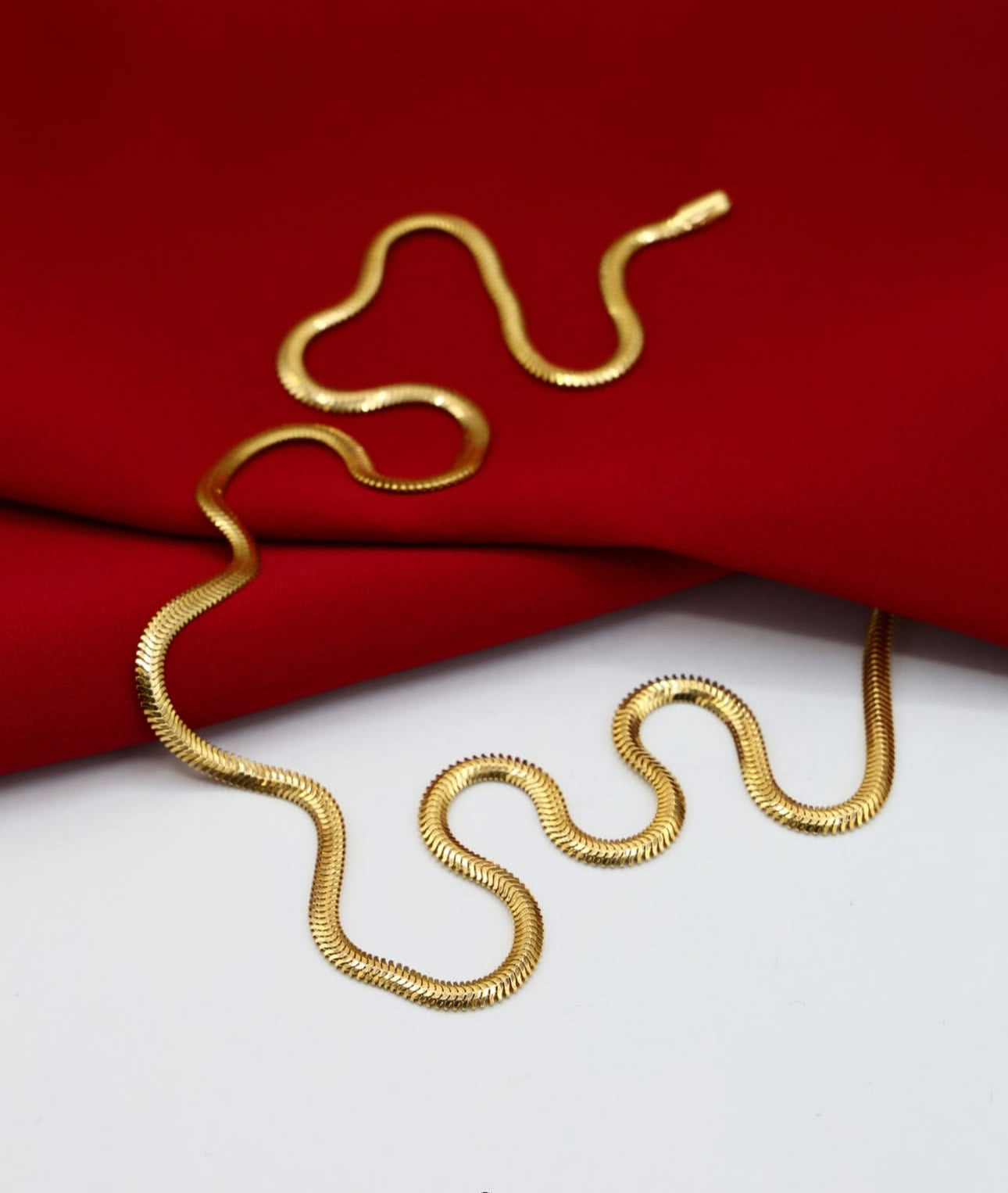 Feine Halskette aus 18k Gelbgold in eleganter Schlangenketten-Form, glänzend und geschmeidig auf rotem Stoff drapiert.