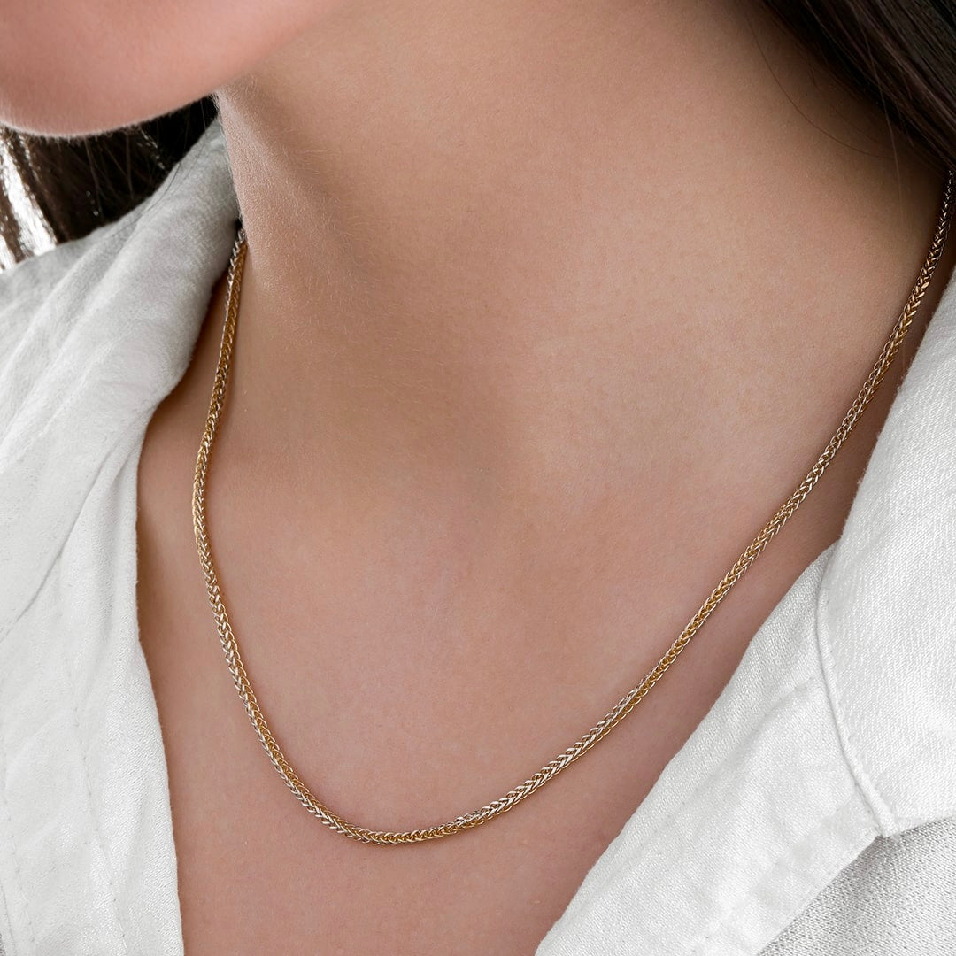 Nahaufnahme einer zweifarbigen Mirokette aus 18k Gelbgold und Weißgold, die locker um den Hals einer Frau liegt. Die feine, dicht verflochtene Gliederstruktur kombiniert warmen Goldton mit kühlem Silberglanz und erzeugt einen dezenten, eleganten Farbkontrast. Getragen zu einem weißen Oberteil mit offenem Kragen.
