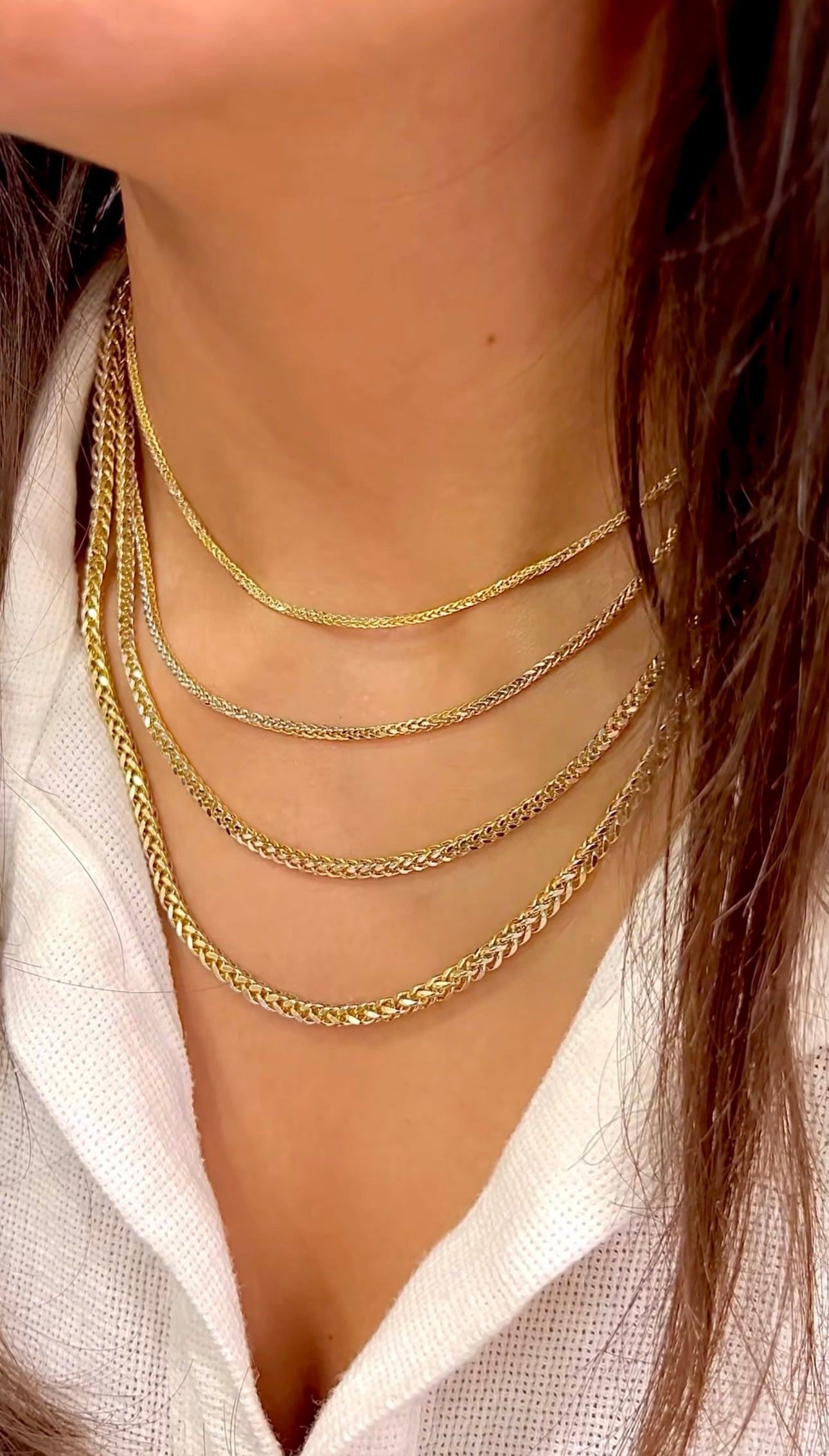 Nahaufnahme mehrerer übereinander getragener Miroketten aus 18k Gelbgold und Weißgold. Die zweifarbigen Ketten („Zanjir-e Miro-ye Tala-ye Dorang“ – Zweifarbige goldene Mirokette) zeigen eine feine, verflochtene Gliederstruktur, bei der warmer Goldton und kühler Weißgoldglanz elegant kombiniert sind. Getragen zu einem weißen, strukturierten Oberteil.