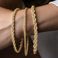 Nahaufnahme eines eleganten Armbands aus 18k Gelbgold – Tanab-e Tala (Goldene Kordel) – mit kunstvoll gedrehter Kordelstruktur, das stilvoll um das Handgelenk einer Person gelegt ist.