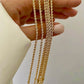 Nahaufnahme mehrerer Armbänder aus 18k Gelbgold in gedrehter Kordeloptik, die locker über die Finger einer Hand gelegt sind. Die polierten, spiralförmig verflochtenen Glieder reflektieren das Licht und erzeugen einen intensiven Goldglanz. Hintergrund neutral und hell, Hand in weißem Stoffärmel.