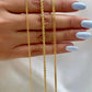 Drei feine Armbänder aus 18k Gelbgold auf einer Hand mit hellblau lackierten Nägeln – links schlicht, in der Mitte gedreht als goldene Kordel (Tanab-e Tala), rechts flachgliedrig.