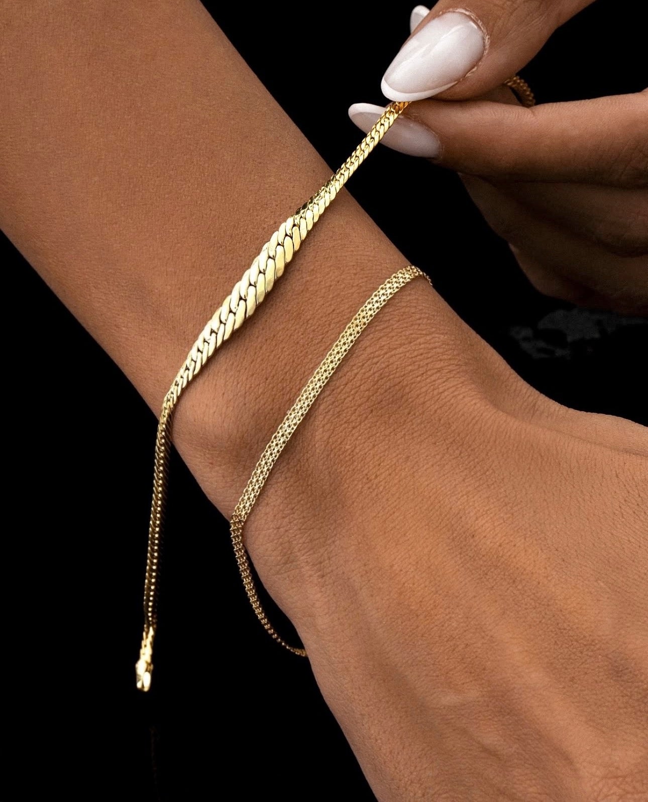 Goldarmband Khat-e Bâfteh aus 18k Gelbgold mit flach geflochtener Struktur – getragen am Handgelenk, elegant kombiniert mit feiner Kette