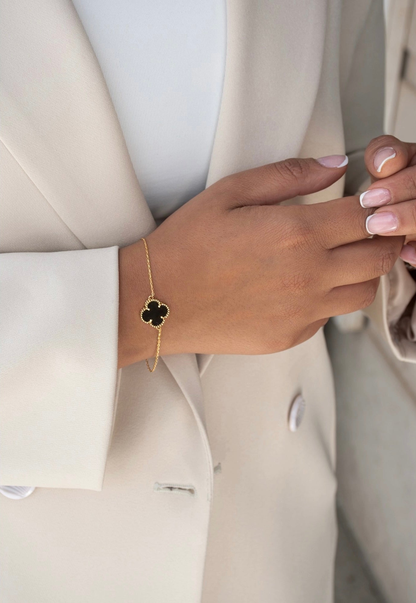 Zweifarbiges Kleeblatt-Armband Shabdar-e Do Rang aus 18k Gelbgold mit schwarzem Inlay – getragen am Handgelenk zu hellem Blazer