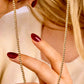 Nahaufnahme von Händen mit dunkelrotem Nagellack, die eine 18k Gelbgold-Perlenkette mit gleichmäßig angeordneten, polierten Goldkugeln halten, vor einem weichen, beigefarbenen Hintergrund.