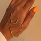 Nahaufnahme einer Goldperlenkette aus 18k Gelbgold, locker über eine Hand mit orange lackiertem Daumennagel gelegt. Die Kette kombiniert polierte Goldperlenabschnitte mit länglichen, feingliedrigen Kettengliedern, was ihr einen modernen, verspielten Look verleiht. Hintergrund in warmem Beigeton.