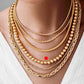 Goldperlenkette aus 18k Gelbgold im Layering-Look getragen, kombiniert mit weiteren Ketten auf heller Haut und weißem Oberteil, markiert für Fokus