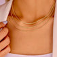 Nahaufnahme eines Halses mit drei filigranen 18k Gelbgold-Kordelketten in unterschiedlichen Längen, übereinander getragen, kombiniert mit einem weißen Blazer und einem hellen Stricktop.
