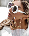 Frau mit weißen, runden Dior-Sonnenbrillen und weißen Nägeln, trägt mehrere 18k Gelbgold-Ringe im Design „Gereh-e Tala“ (Goldener Knoten) an verschiedenen Fingern, stilvoll kombiniert mit einem weißen Outfit.